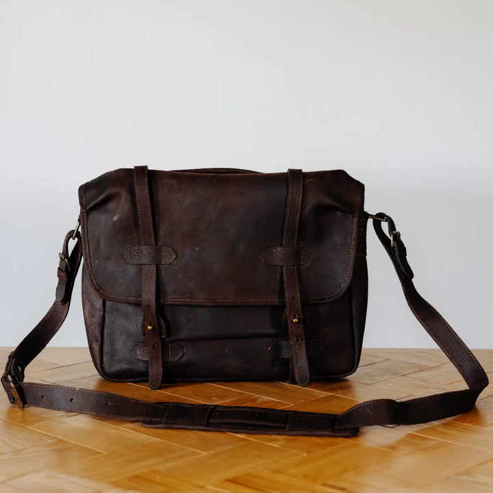 Brown boar leather messgener bag on a wooden surface with a light gray background