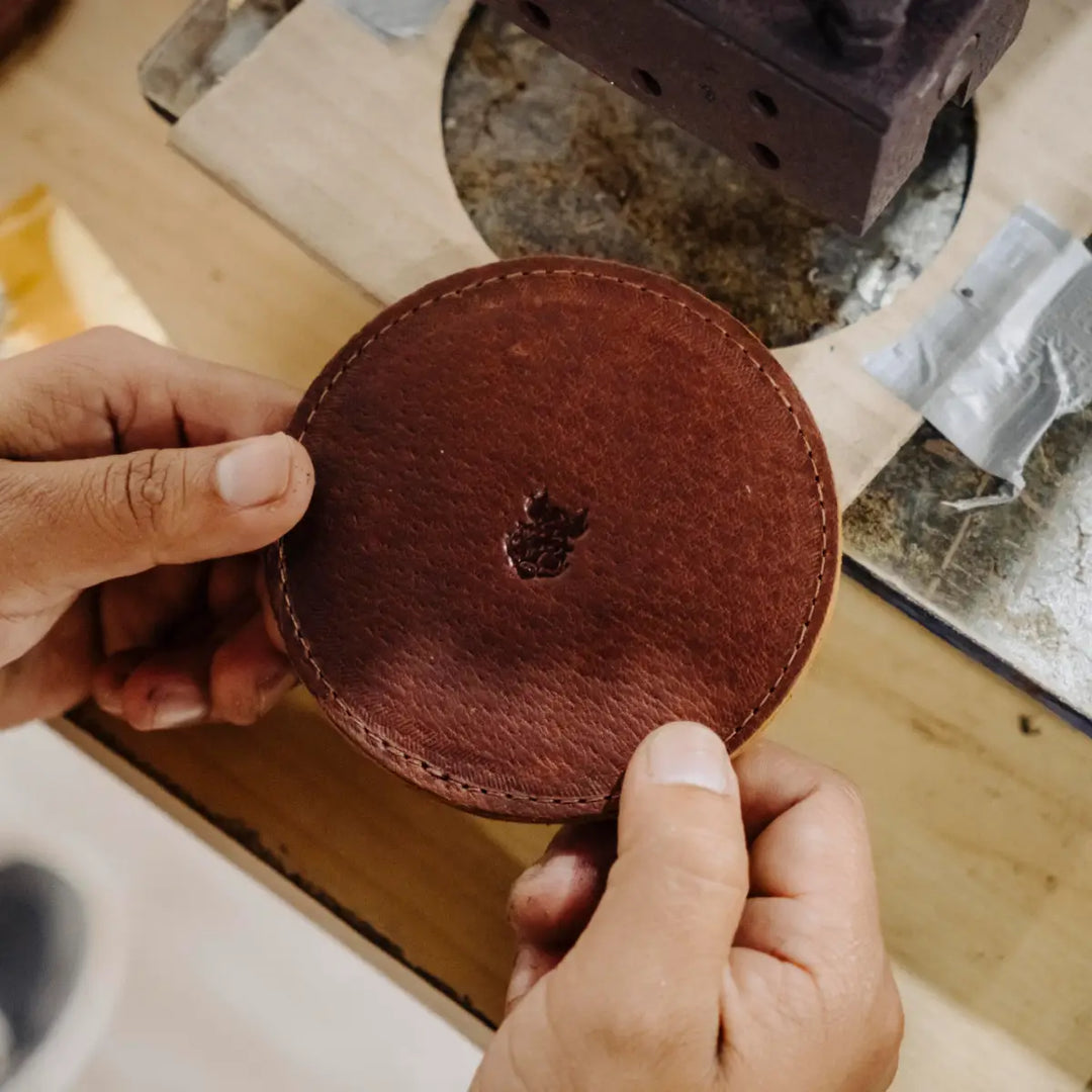 Person holding a brown leather coaster with a sewing machine in the background