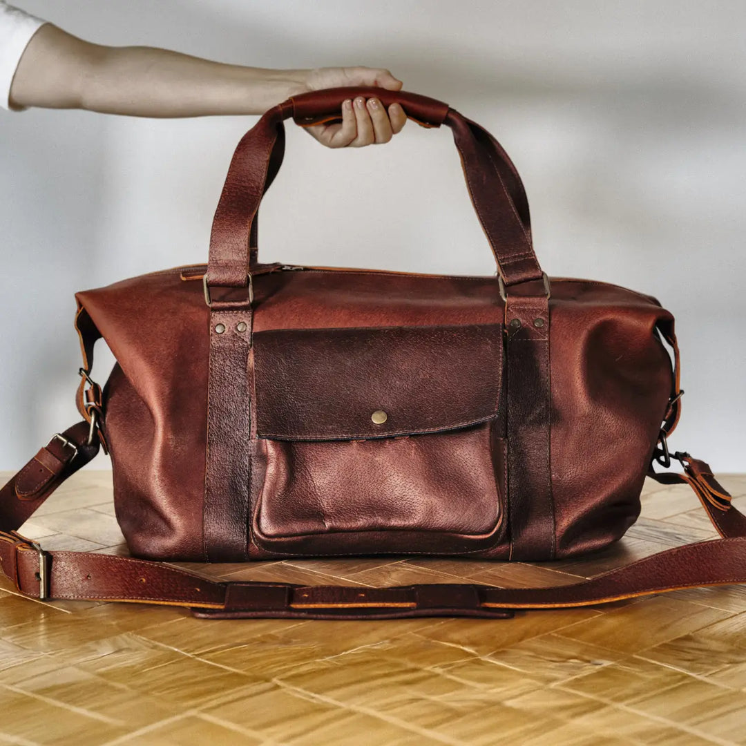 Brown boar leather duffel bag on a wooden floor with a neutral background