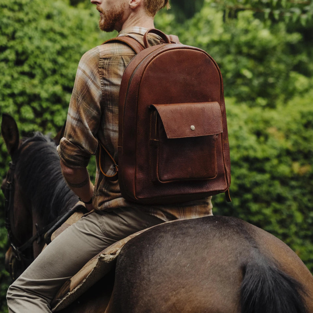 Man riding a horse wearing a brown  cognac jabari boar leather backpack in a forest setting