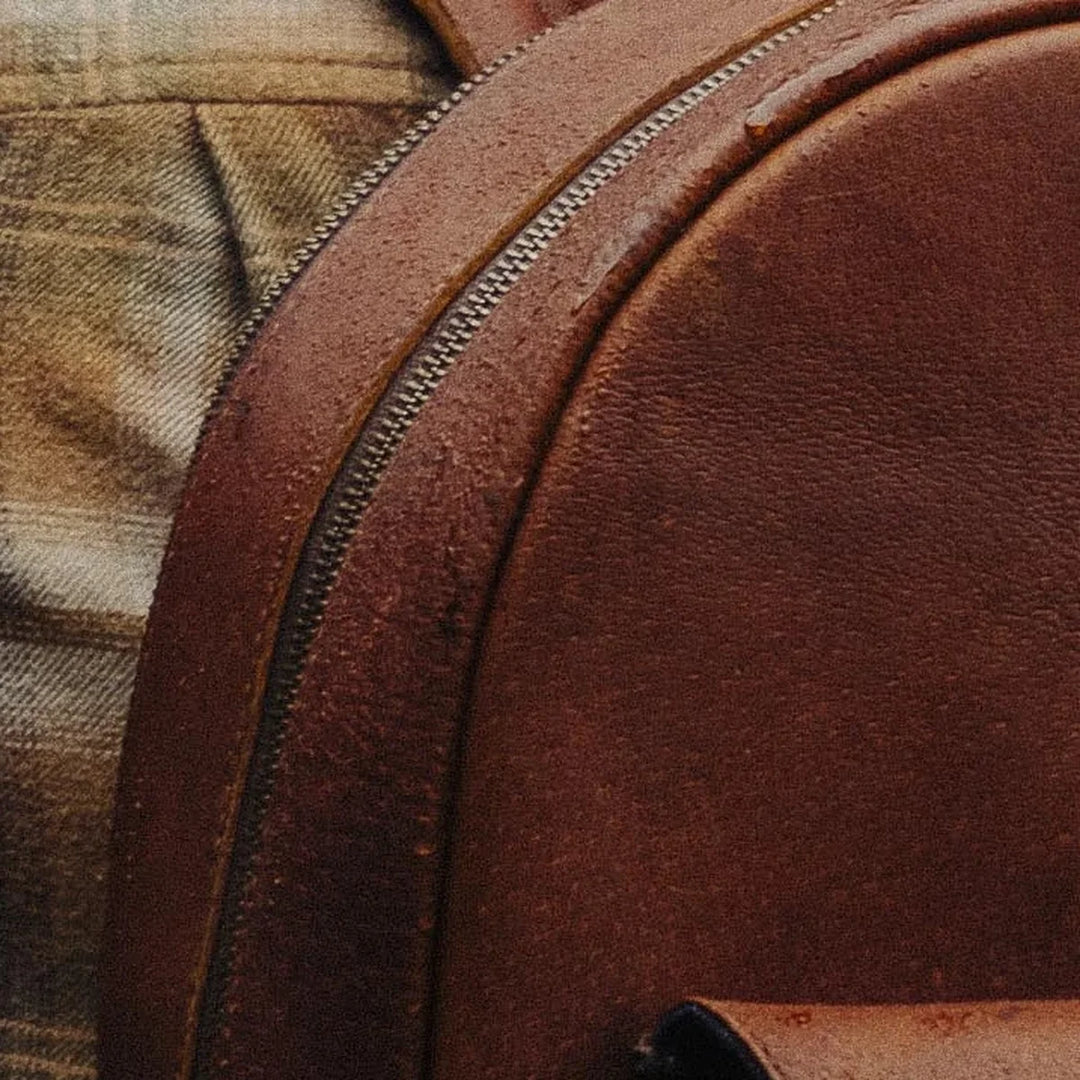 Close-up of a brown Cognac Jabari leather backpack with a zipper and water beading off the leather
