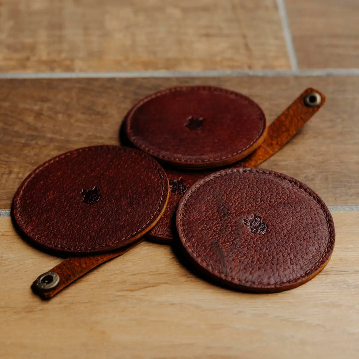 Three brown leather coasters with straps on a wooden surface