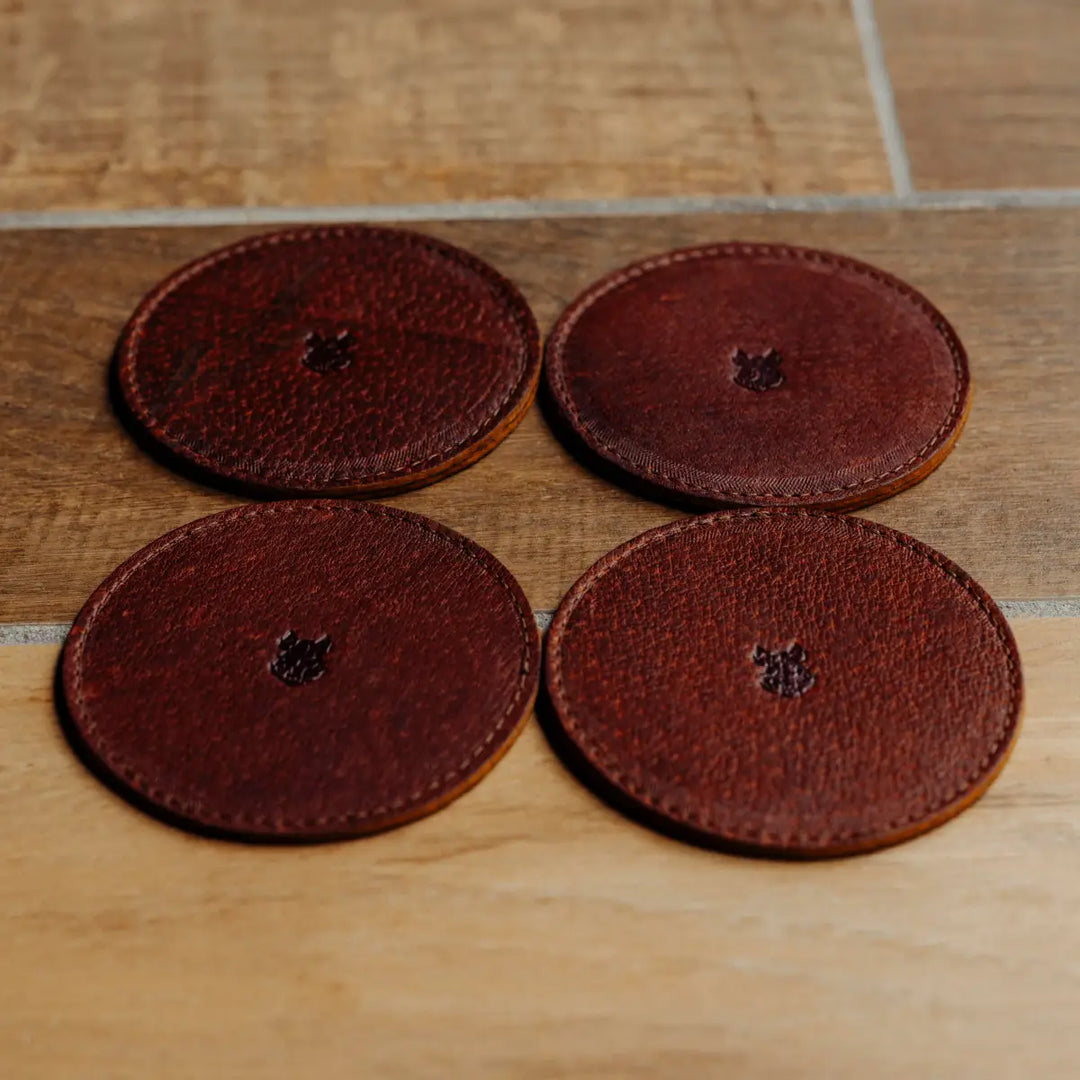 Four brown leather coasters on a wooden surface