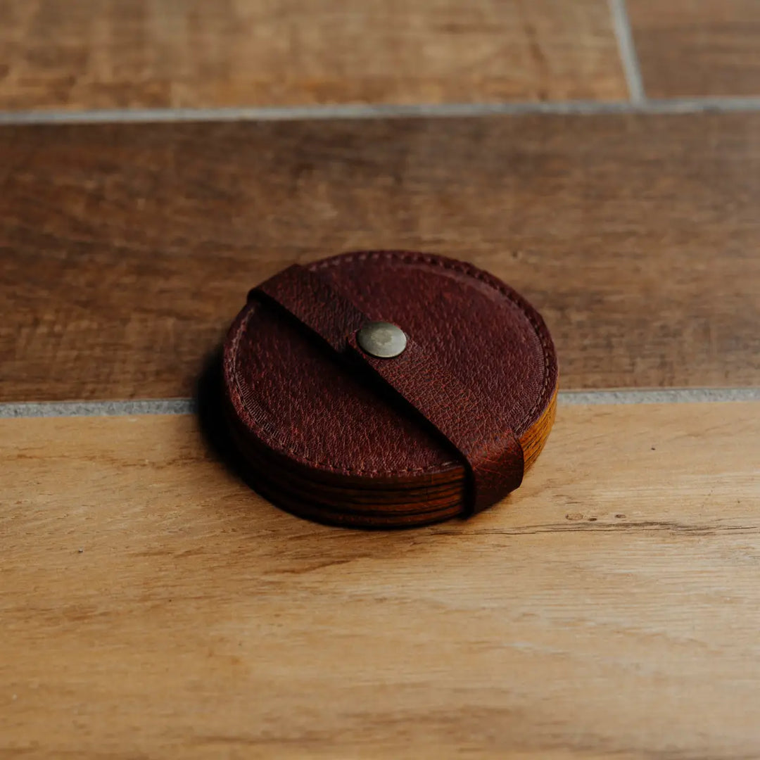 Round brown leather coaster with a central button on a wooden surface