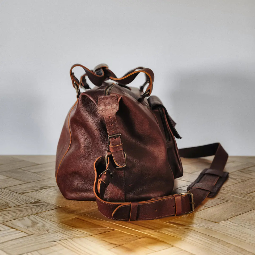 The side synches of a brown boar leather bag on a wooden surface with a neutral background