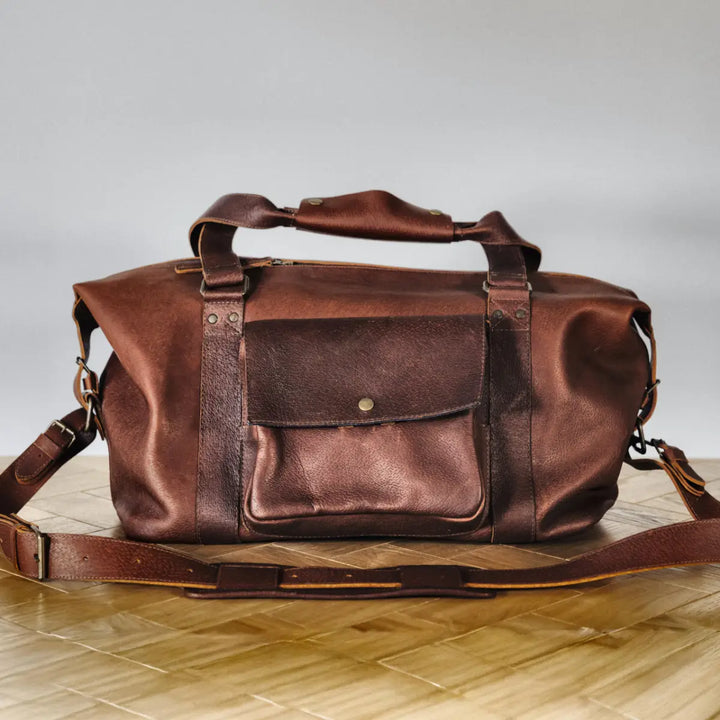Brown boar leather duffel bag on a wooden surface with a neutral background