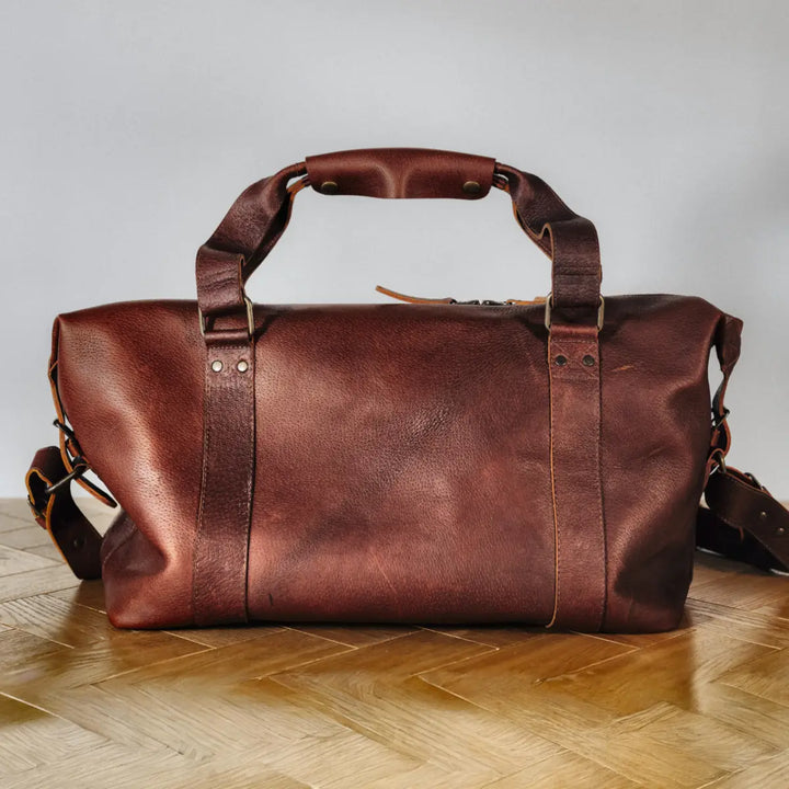 Brown boar leather duffel bag on a wooden floor with a neutral background