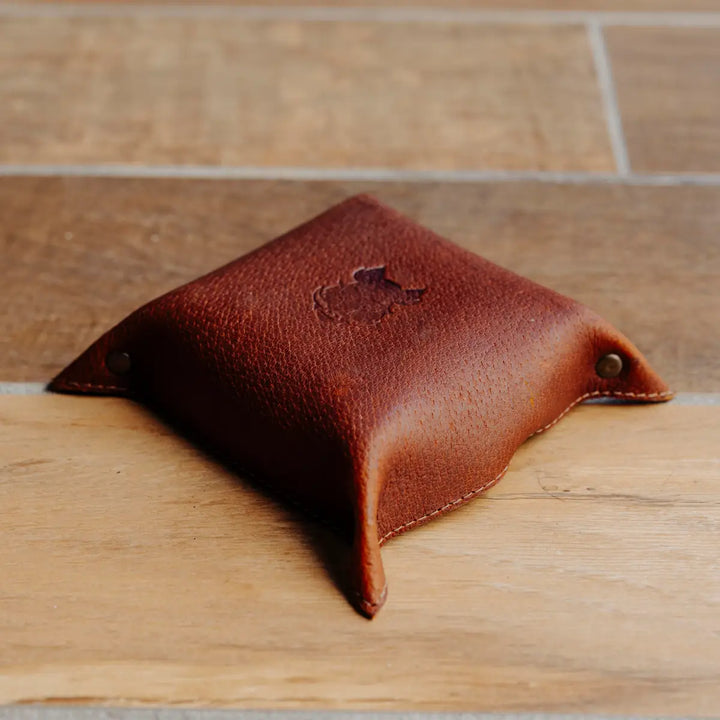 Cognac boar leather valet tray on a wooden surface with a blurred background