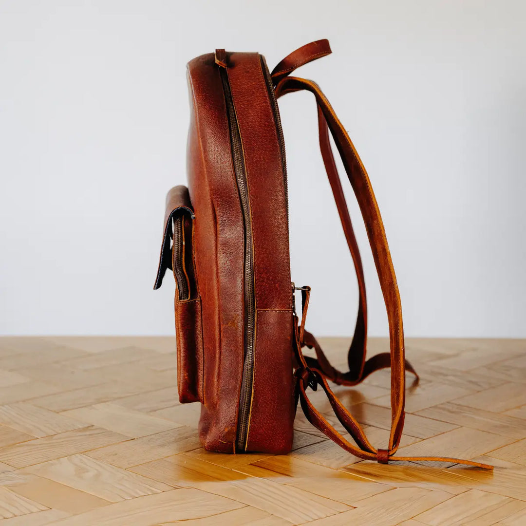 Cognac leather backpack on a wooden floor with a white wall background