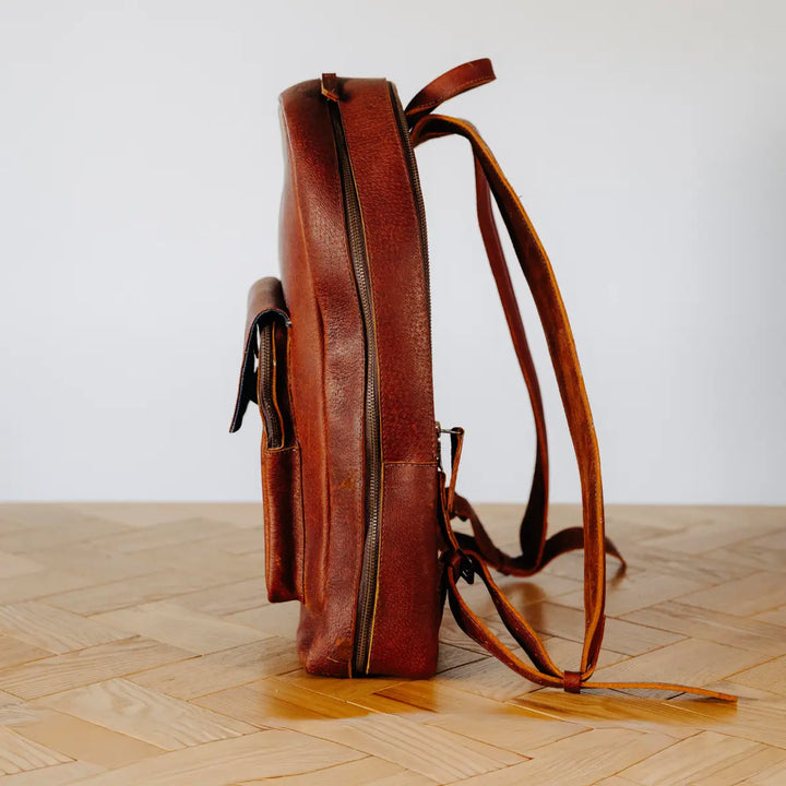 Cognac leather backpack on a wooden floor with a white wall background