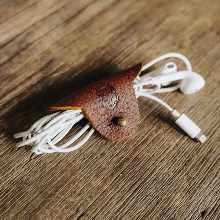 brown cognac Jabari leather cable and earbud holder with white earbuds on a wooden surface