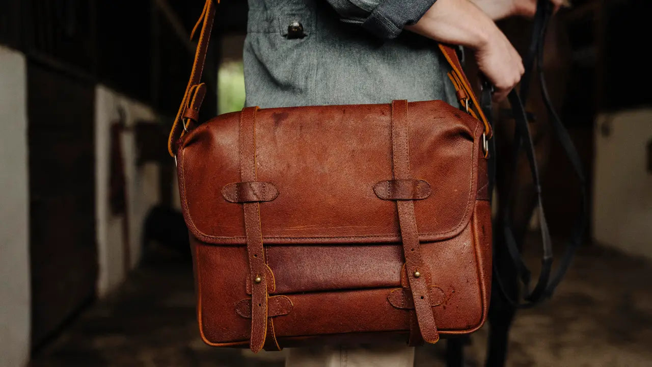Brown cognac jabari boar leather messenger held by a person with a blurred background