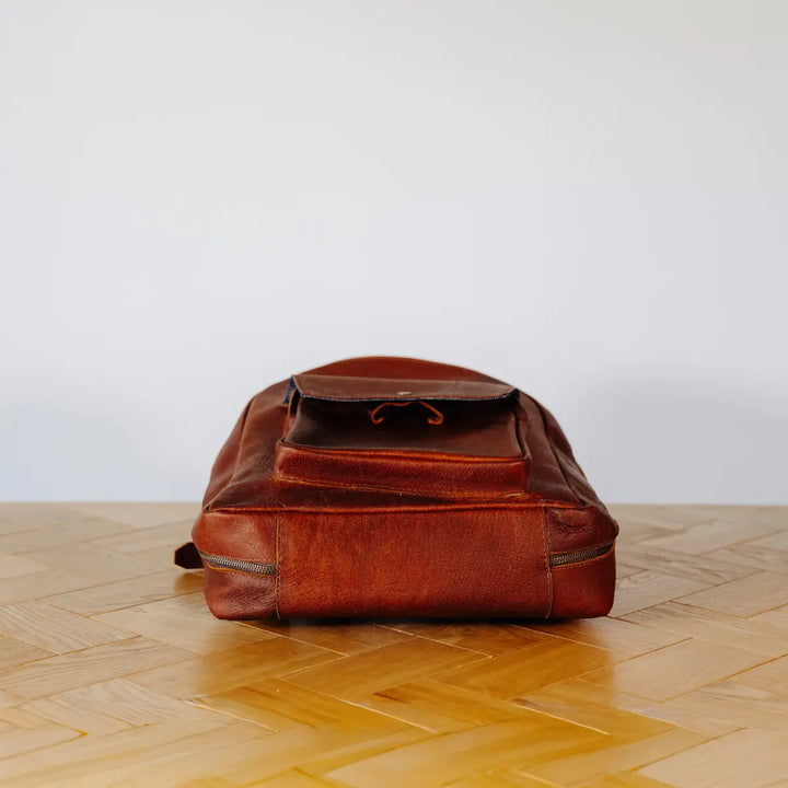 Brown leather backpack on a wooden floor with a white wall background