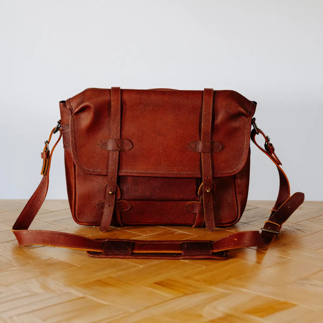 Brown boar leather messenger bag on a wooden surface with a light gray background
