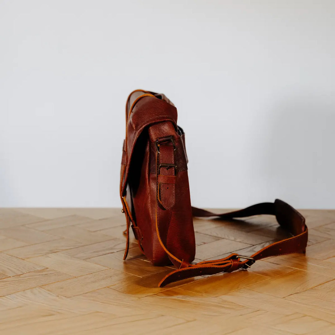 Brown boar leather bag on a wooden floor with a white background