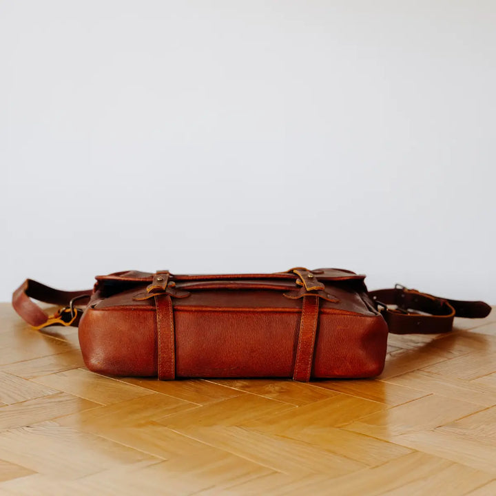 Brown boar leather bag on a wooden floor with a light gray background