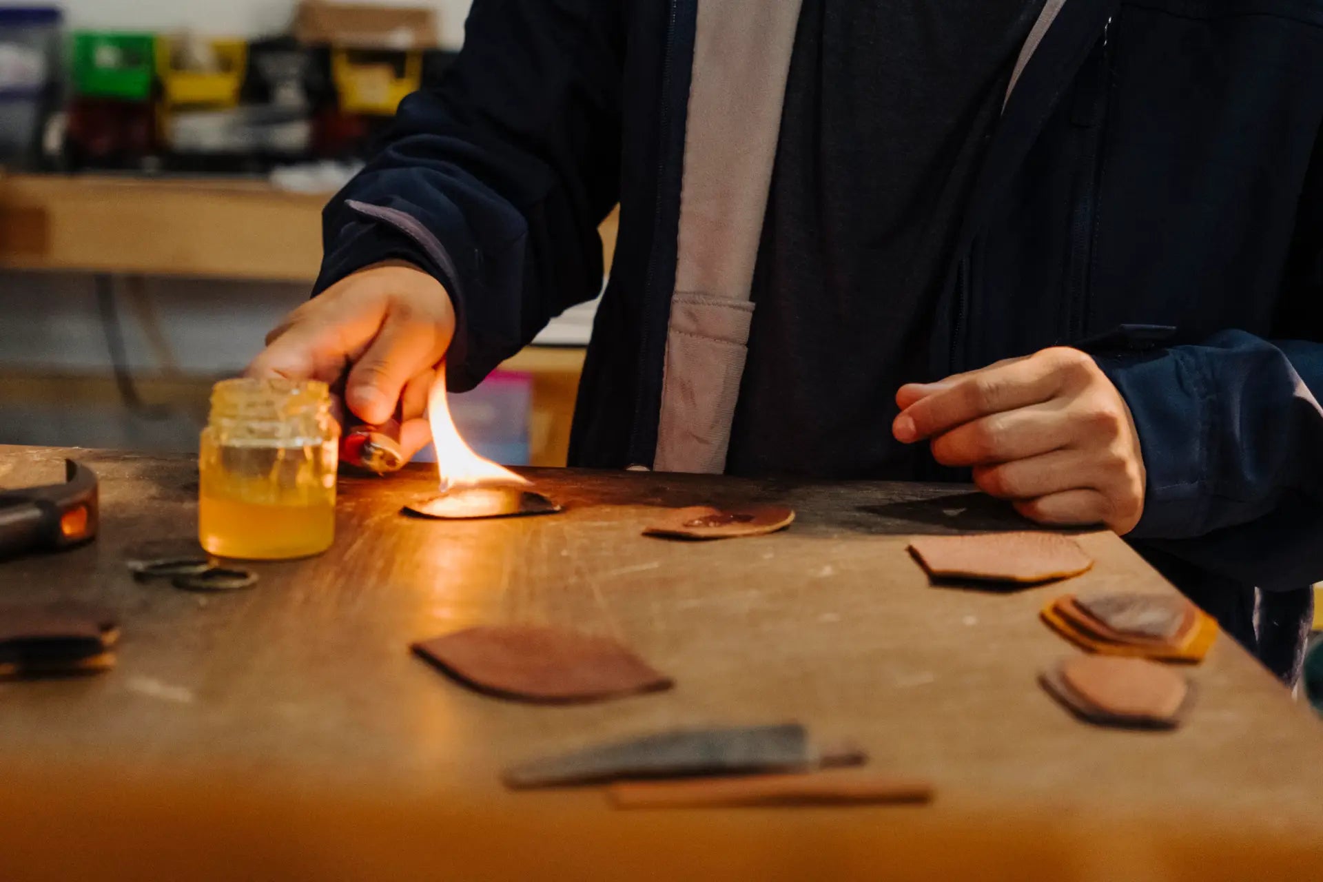 Person lighting a small flame with a wooden table and leather pieces in the foreground