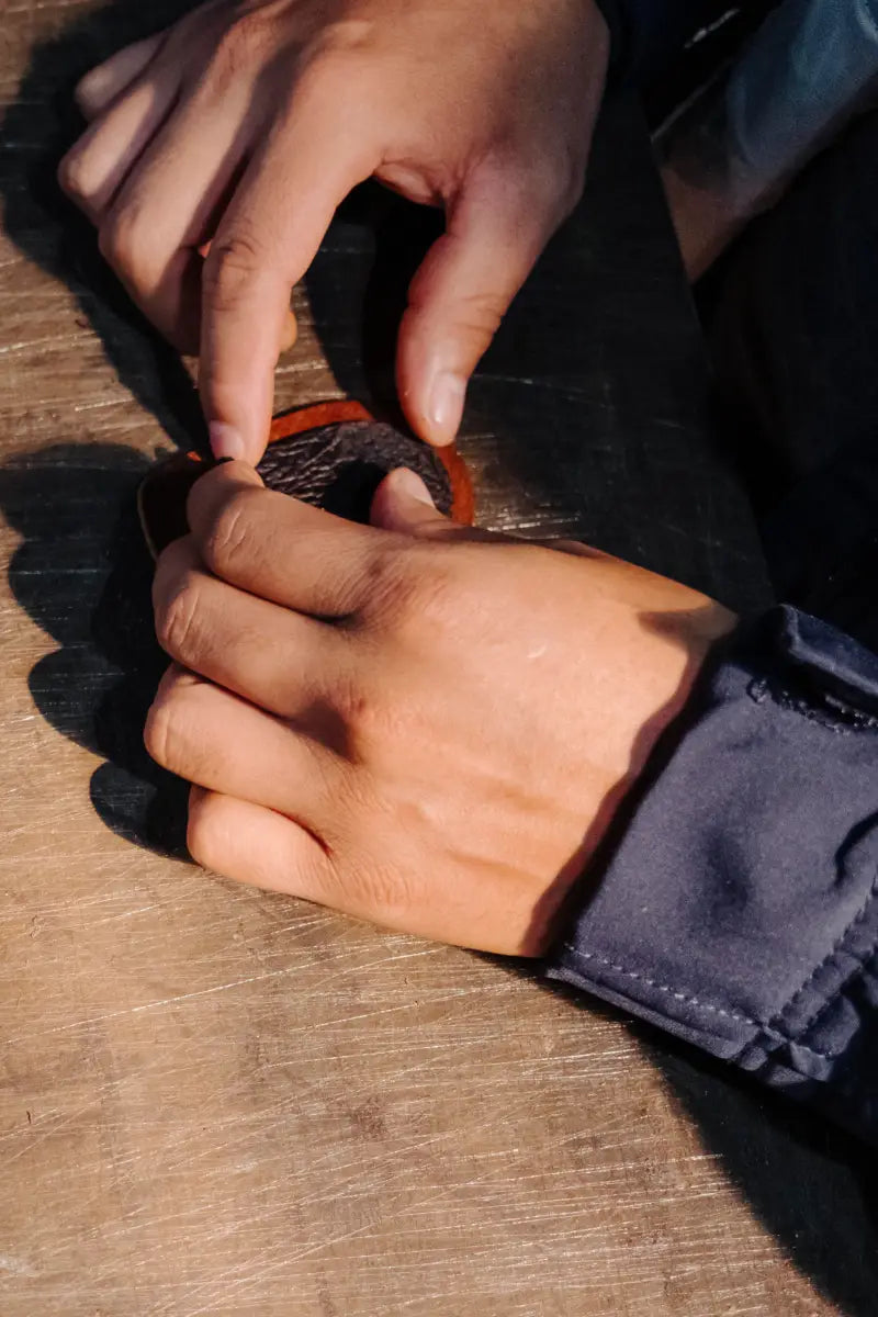 Close-up of two hands working on a leather project on a wooden surface