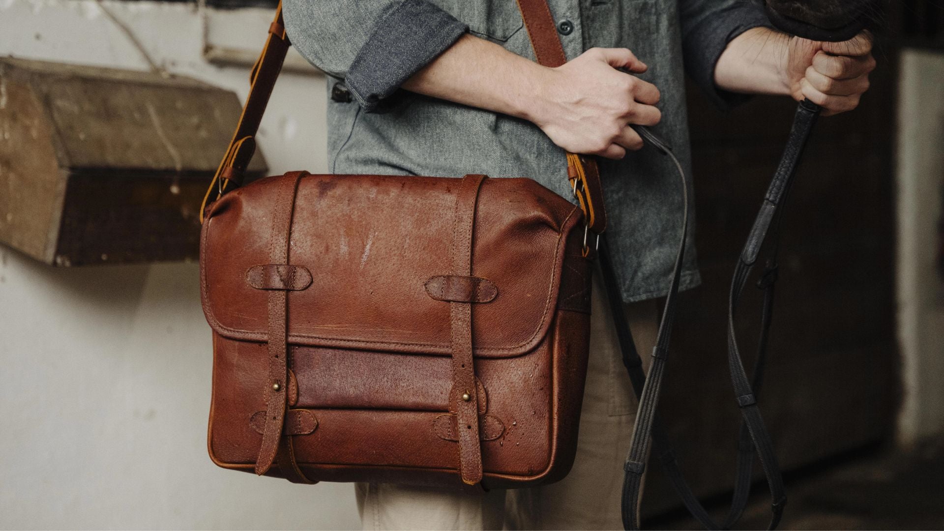 Brown leather satchel bag held by a person with a blurred background