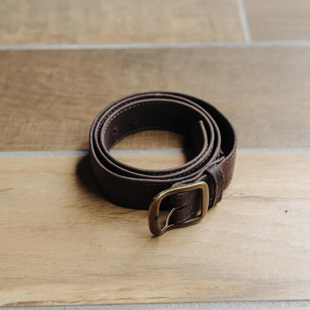 Brown leather belt with brass buckle on a wooden surface