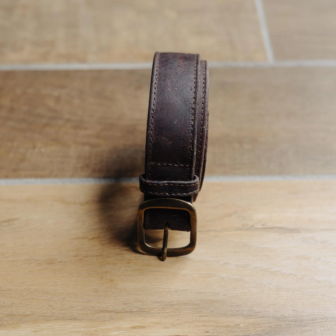 Brown leather belt with a brass buckle on a wooden surface