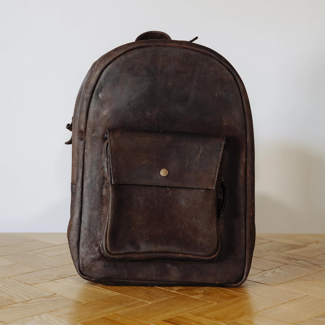 Brown leather backpack on a wooden floor with a white wall background