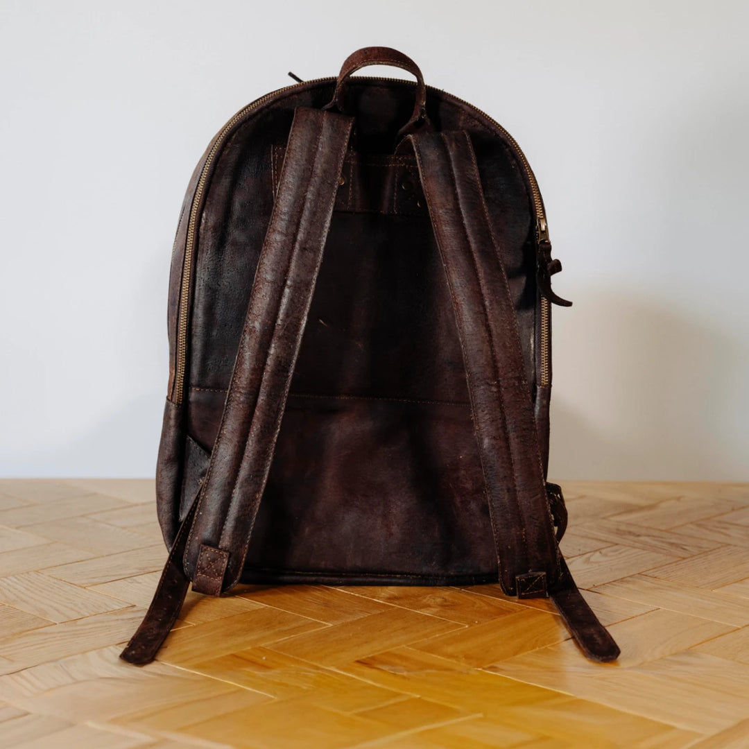 Brown leather backpack on a wooden floor with a white wall background