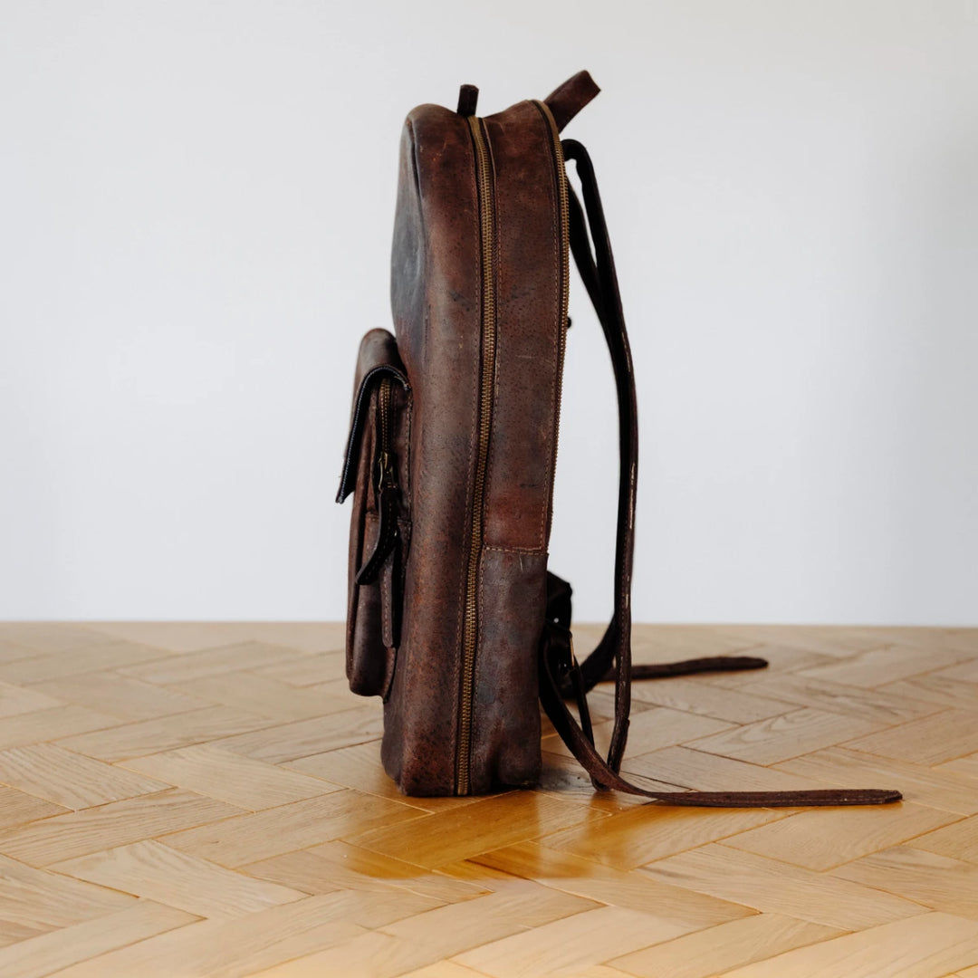 Brown leather backpack on a wooden floor with a white wall background