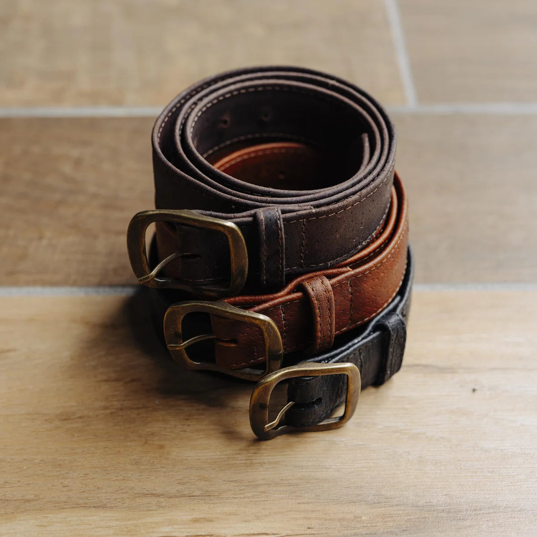 Two brown leather belts and one black leather belt with brass buckles on a wooden surface.
