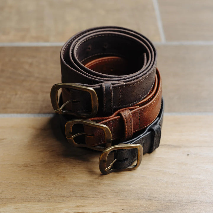 Two brown leather belts and one black leather belt with brass buckles on a wooden surface.
